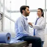 A man sitting on a table getting a medical examination by a female doctor.