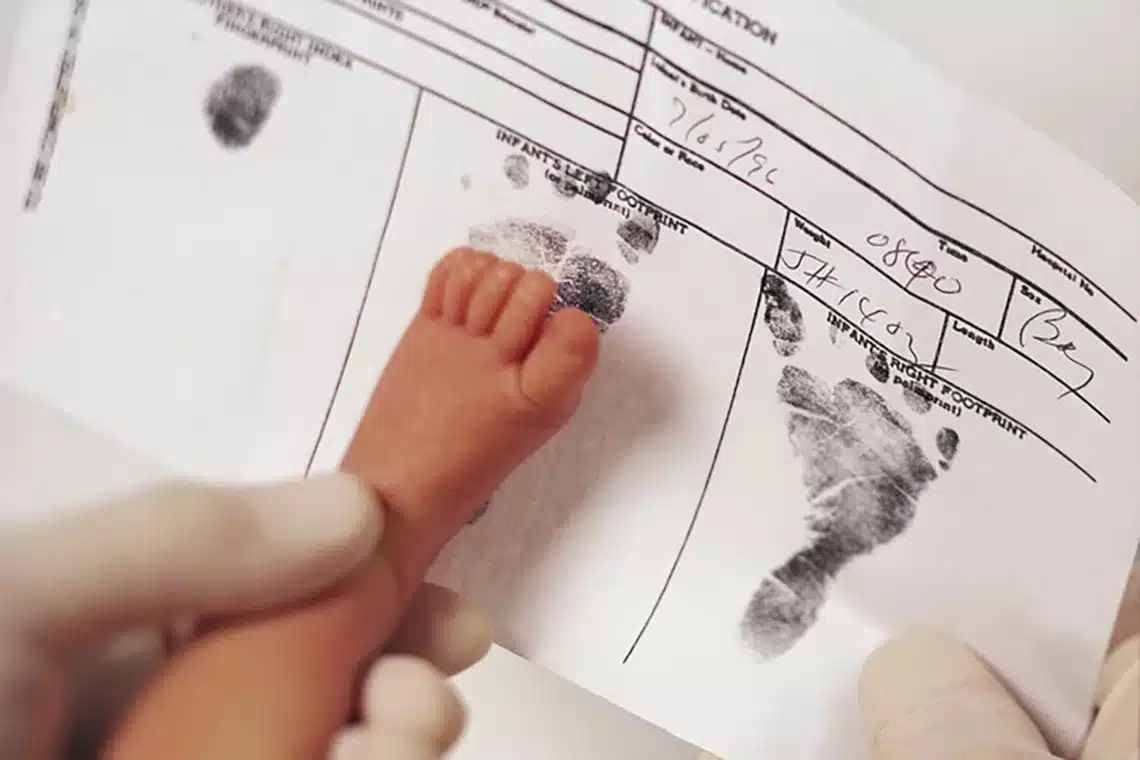 healthcare worker holding the foot of a newborn to obtain a footprint of on a birth certificate