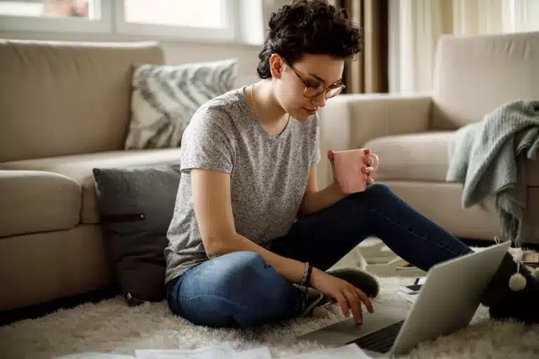 A woman sitting in her living room with a cup of coffee browsing frequently asked questions online.