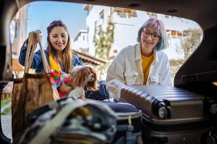 Two females and a dog packing up the back end of a car for a trip to Arkansas.